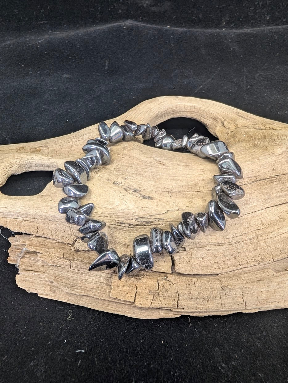 Full view of a metallic gunmetal-grey Hematite chip bracelet on a natural driftwood base, highlighting its heavy luster.