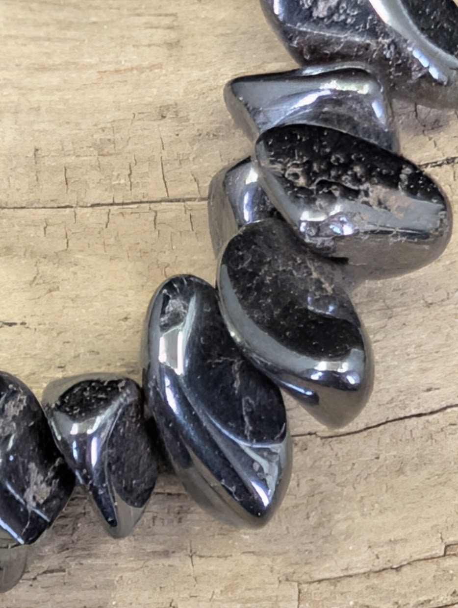 Extreme macro shot of tumbled Hematite chips, emphasizing the dense, mirror-like polish and characteristic steel-grey color zoning.