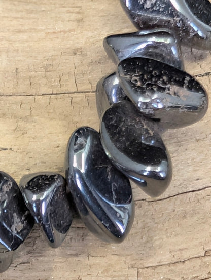 Extreme macro shot of tumbled Hematite chips, emphasizing the dense, mirror-like polish and characteristic steel-grey color zoning.