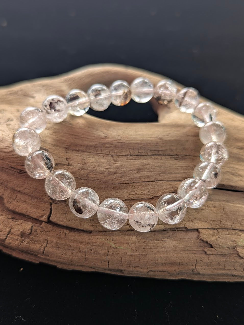 Intuitively selected 11mm AAA Grade Himalayan Garden Quartz beaded stretch bracelet resting on driftwood, showcasing excellent optical clarity.