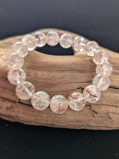 Intuitively selected 12mm AAA Grade Himalayan Garden Quartz beaded stretch bracelet displayed on driftwood, showing highly transparent high-altitude quartz.
