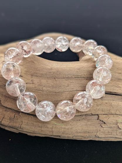 Intuitively selected 13mm AAA Grade Himalayan Garden Quartz beaded stretch bracelet resting on driftwood, showcasing large, collector-grade spheres.