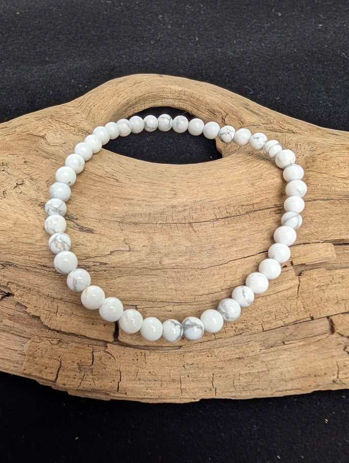 4mm smooth Howlite beaded stretch bracelet resting on a driftwood display, showing a porcelain-white base with dark grey veining.