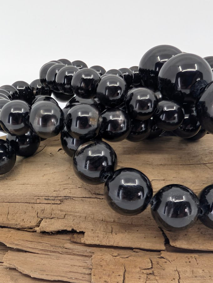 Close-up of Hypersthene beads on wood highlighting glossy polish and silver internal reflections