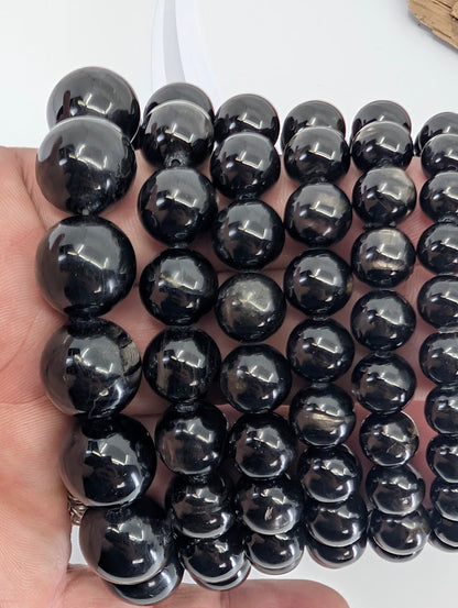 Multiple Hypersthene bracelets held in hand showing bead size variations and strong sheen