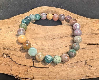 Faceted 8mm Indian Agate beaded bracelet resting on natural driftwood, showcasing a natural mix of earthy green, red, tan, and purple colours.