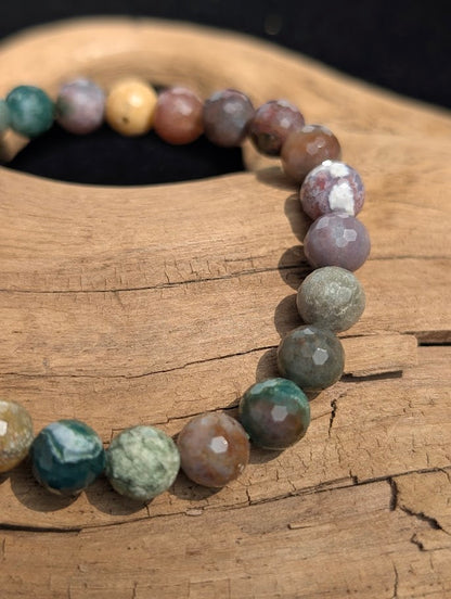 Macro view of faceted 8mm Indian Agate beads on driftwood, displaying crisp lapidary cuts and natural chalcedony colour zoning.