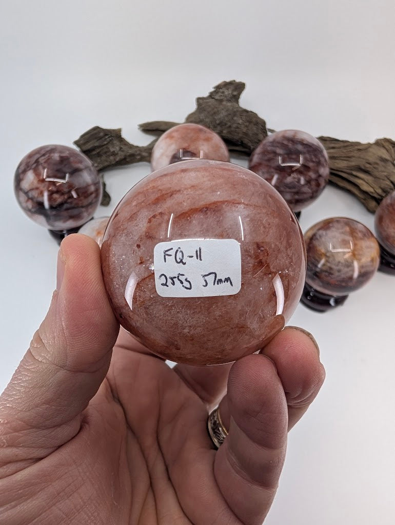 Collector hand scale verification photo of Brazilian Hematoid Quartz sphere FQ-11, showing the tracking label marked 255 grams and 57mm.