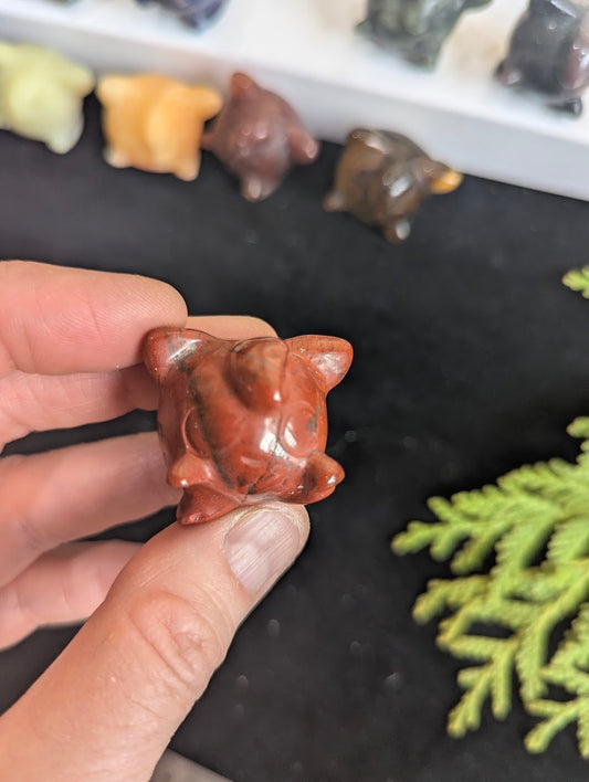 Frontal view of a 3cm Jigglypuff carved from natural Red Jasper held in hand.