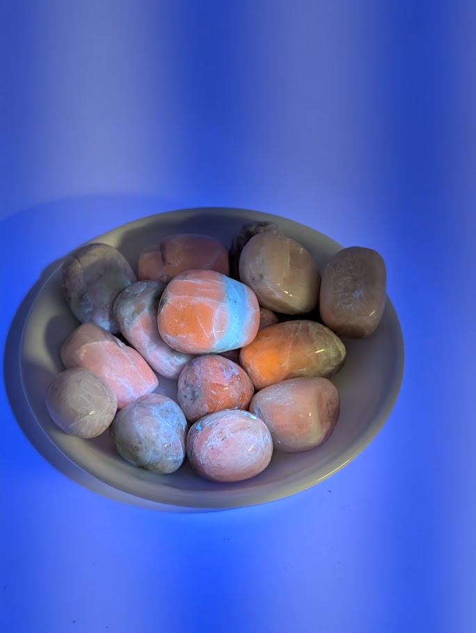 Kunzite tumbled stones fluorescing orange-pink under UV light
