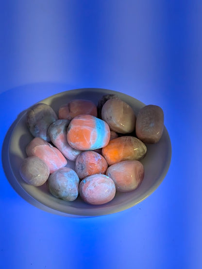 Kunzite tumbled stones fluorescing orange-pink under UV light
