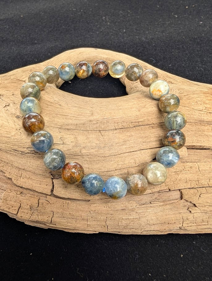 8mm smooth Kyanite beaded stretch bracelet resting on a driftwood display, showing earthy denim blue, silver, and brown colouration.