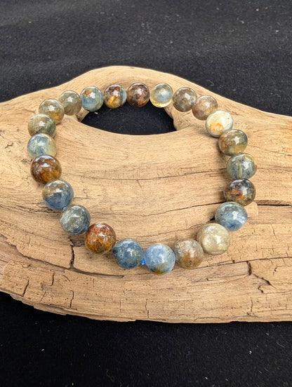 8mm smooth Kyanite beaded stretch bracelet resting on a driftwood display, showing earthy denim blue, silver, and brown colouration.