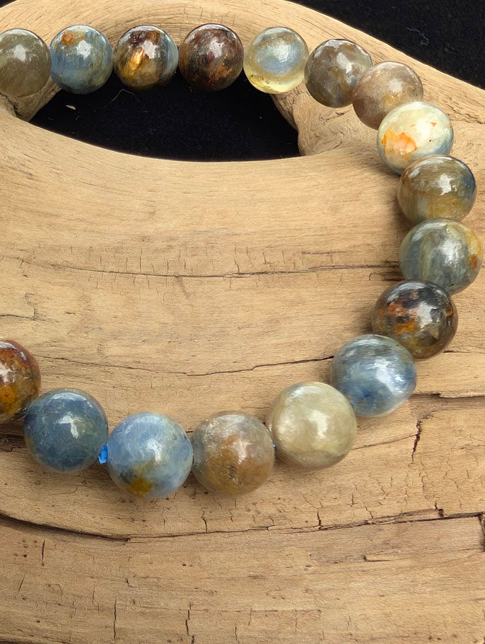 Macro close-up of 8mm smooth Kyanite beads highlighting bladed internal structures, natural earthy iron inclusions, and a blue stretch cord.