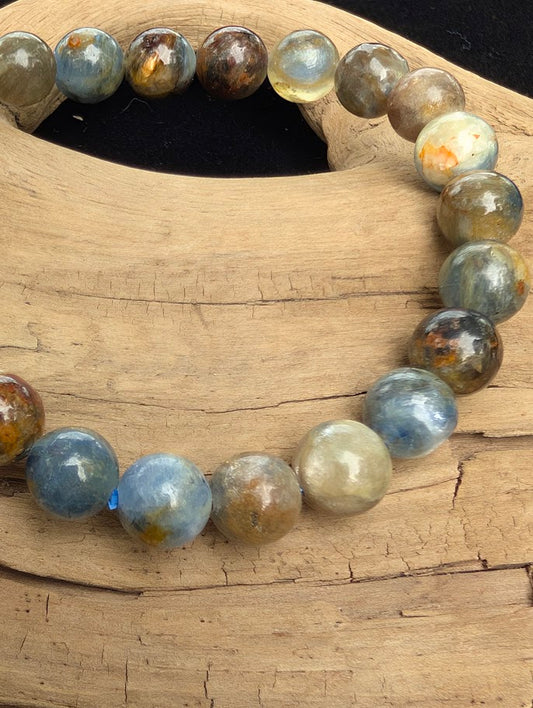Macro close-up of 8mm smooth Kyanite beads highlighting bladed internal structures, natural earthy iron inclusions, and a blue stretch cord.
