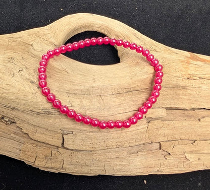 4mm polished lab-grown Ruby beaded stretch bracelet resting on a driftwood display, showing vibrant magenta-red colouration.