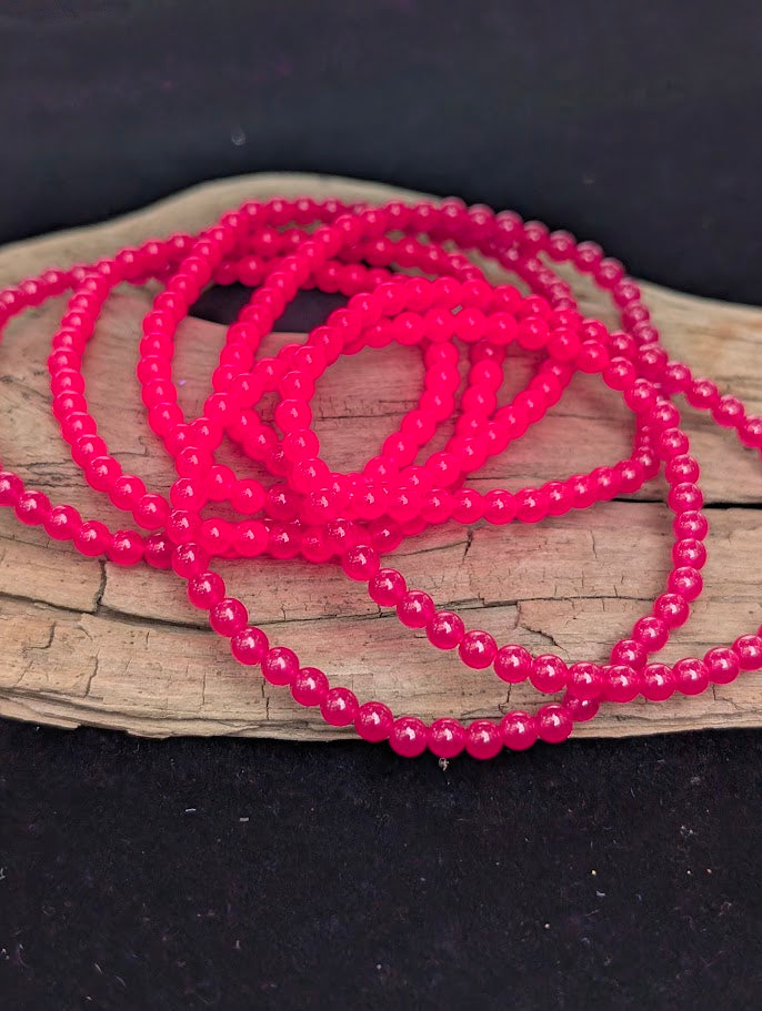 Multiple 4mm polished lab-grown Ruby beaded stretch bracelets tangled together resting on a driftwood display under a UV light.