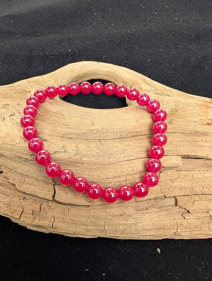 6mm polished lab-grown Ruby beaded stretch bracelet resting on a driftwood display from a top-down angle.