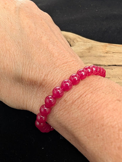 6mm polished lab-grown Ruby beaded stretch bracelet worn on a wrist for delicate size scale.