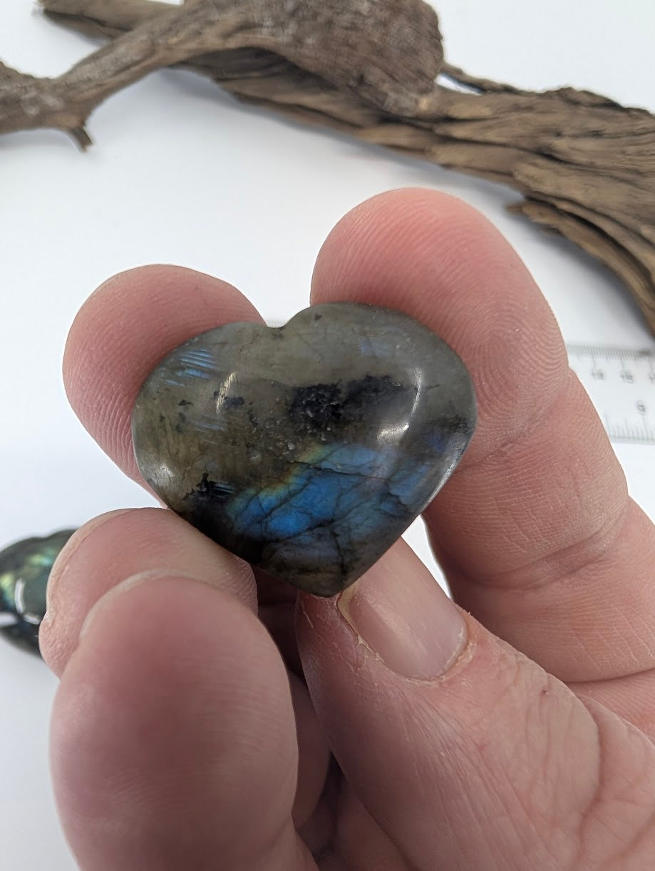 Fingers holding a tiny 10g Labradorite heart showing gold and blue flash.