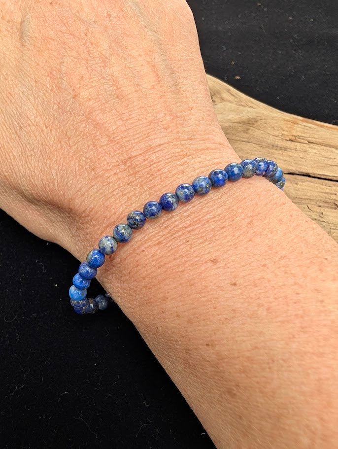 4mm polished Lapis Lazuli beaded stretch bracelet resting on a driftwood display, showing royal blue tones and natural pyrite inclusions.