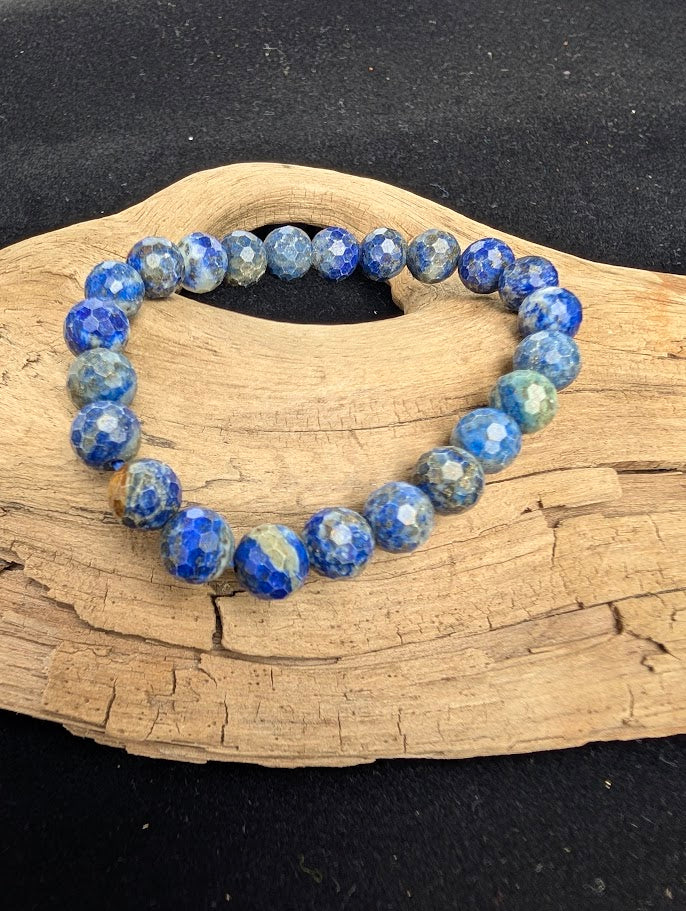 8mm faceted Lapis Lazuli beaded stretch bracelet resting on a driftwood display, showing deep celestial blue, white calcite, and golden pyrite colouration.