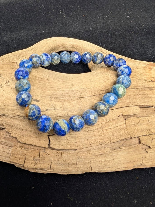 8mm faceted Lapis Lazuli beaded stretch bracelet resting on a driftwood display, showing deep celestial blue, white calcite, and golden pyrite colouration.