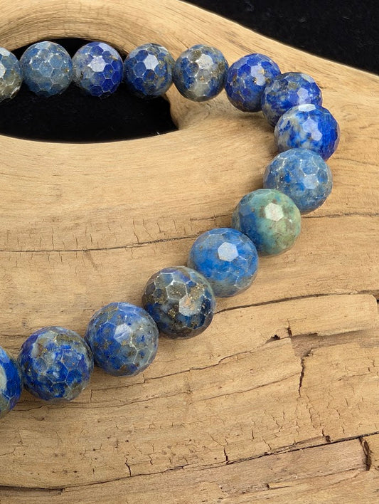 Macro close-up of 8mm faceted Lapis Lazuli beads highlighting geometric surface cuts, metallic pyrite flecks, and a blue stretch cord.