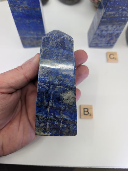 Afghan Lapis Lazuli tower B (LT-02) held in hand, revealing dense lazurite color, significant golden pyrite distribution, and the distinct natural patterns resulting from the aggregate rock formation.