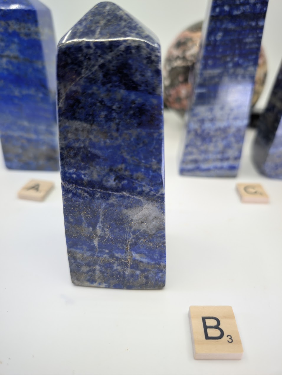 Polished Afghan Lapis Lazuli tower (obelisk) B (LT-02), standing 11cm tall, labeled with Scrabble tile B, showcasing prominent white calcite veining and dispersed golden pyrite flecks against deep blue stone.