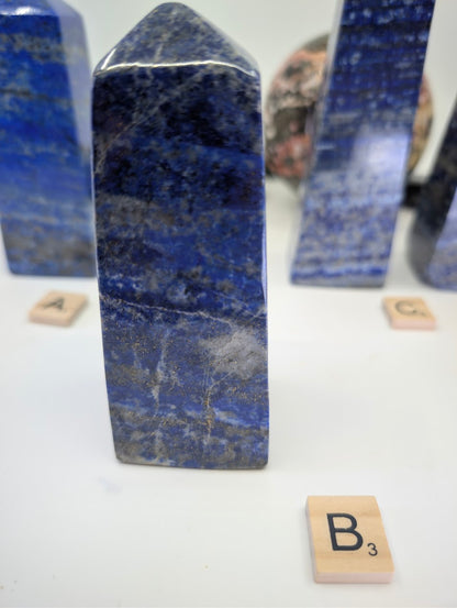 Polished Afghan Lapis Lazuli tower (obelisk) B (LT-02), standing 11cm tall, labeled with Scrabble tile B, showcasing prominent white calcite veining and dispersed golden pyrite flecks against deep blue stone.