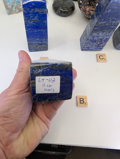 The unpolished, flat base of Lapis Lazuli tower LT-02 from Afghanistan, featuring a white inventory label marked "LT-02, 11cm, 450g", showing the internal rock structure.