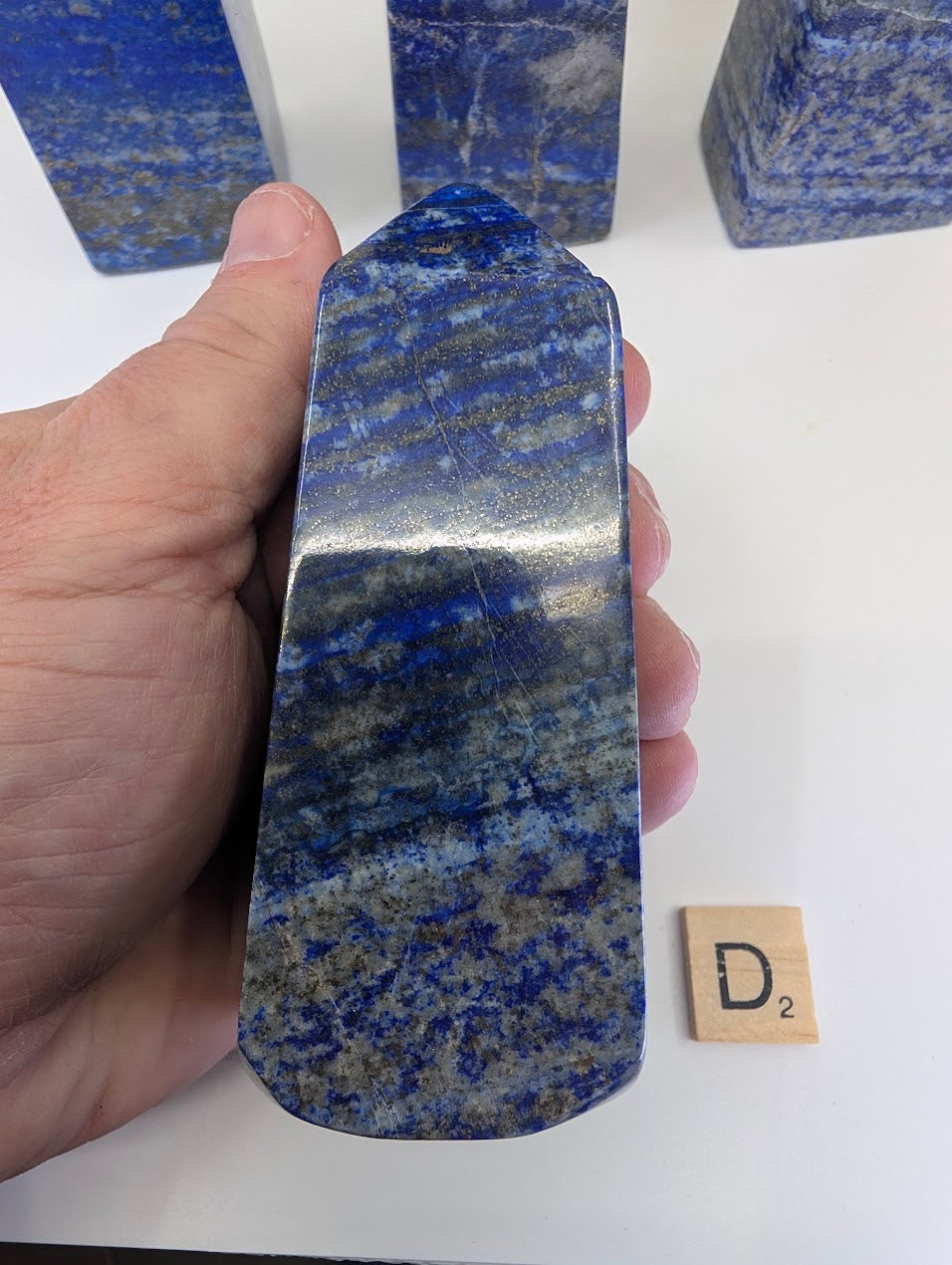 Afghan Lapis Lazuli tower D (LT-04) held in hand, showing a dense distribution of metallic golden pyrite inclusions and marbled white calcite matrix within the vibrant blue lazurite.