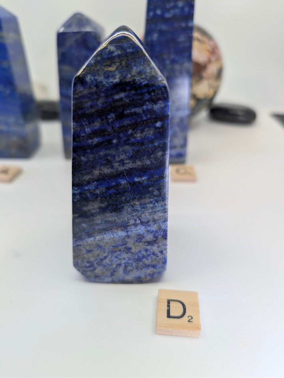 Polished Afghan Lapis Lazuli tower D (LT-04), standing 11cm tall, labeled with Scrabble tile D, featuring complex, wavy patterns of white calcite and prominent golden pyrite flecks against rich blue stone.