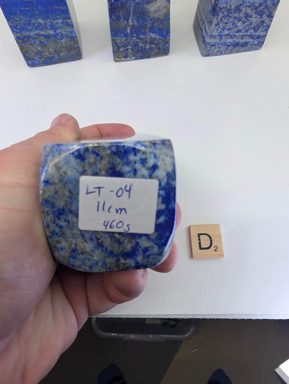 The flat, unpolished base of Lapis Lazuli tower LT-04 from Afghanistan, showing a white handwritten label marked "LT-04, 11cm, 460g" and the natural aggregate crystal structure of the stone.