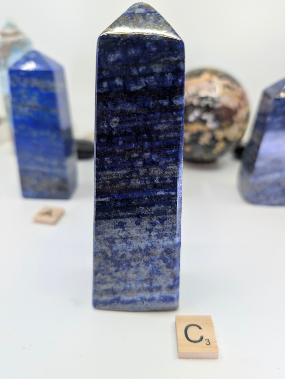 Polished Afghan Lapis Lazuli tower C (LT-03), standing 14cm tall, labeled with Scrabble tile C, featuring a darker blue lazurite matrix at the apex transitioning to heavy white calcite banding at the base.