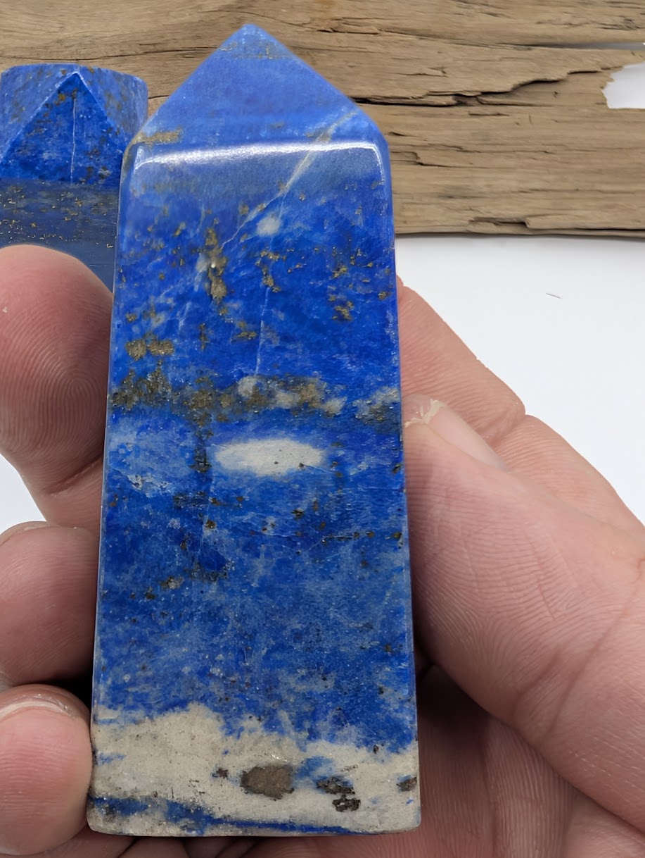 Hand holding a polished Lapis Lazuli tower showing deep blue color with gold pyrite flecks and white calcite base.