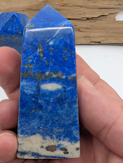 Hand holding a polished Lapis Lazuli tower showing deep blue color with gold pyrite flecks and white calcite base.