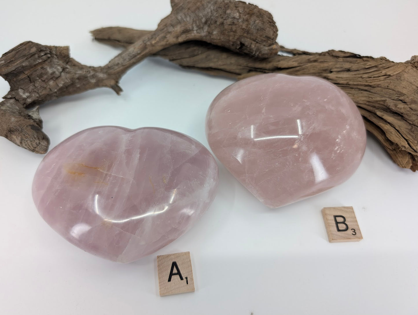 Comparison of two massive Rose Quartz hearts, Specimen A and B, on driftwood.