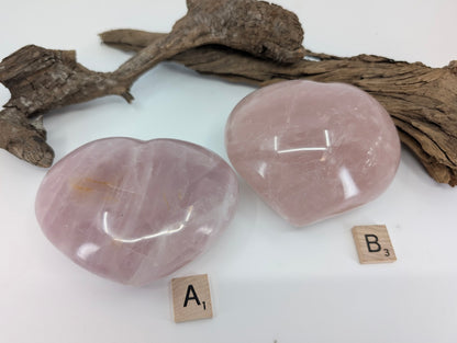 Comparison of two massive Rose Quartz hearts, Specimen A and B, on driftwood.