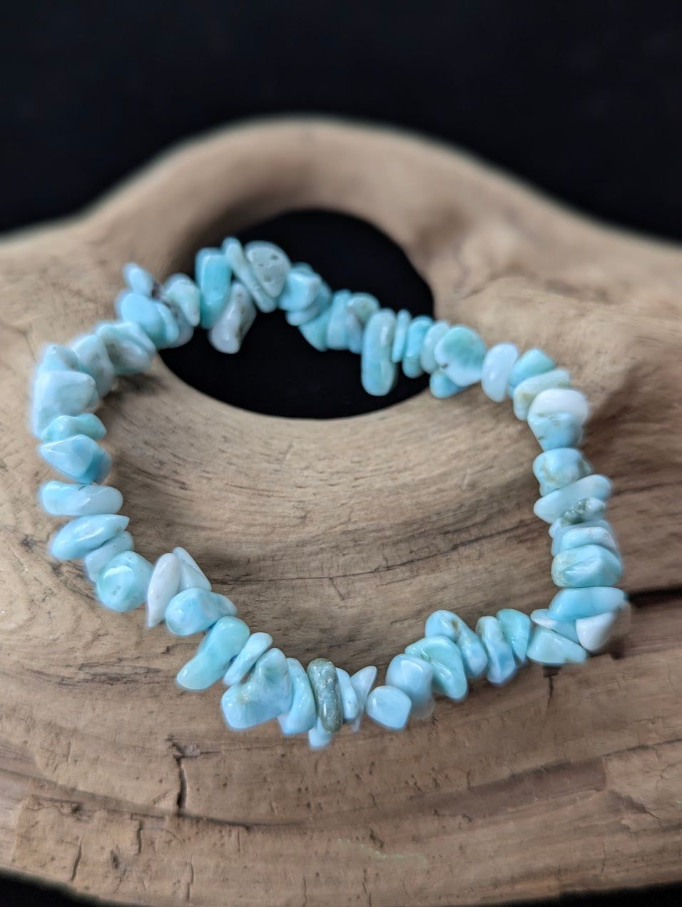 AA Grade natural Larimar chip bracelet from the Dominican Republic resting on natural driftwood, showcasing bright oceanic blue and white patterning.