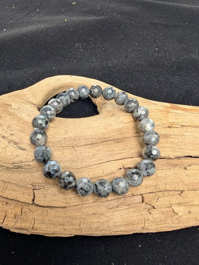 8mm faceted Larvikite beaded stretch bracelet resting on a driftwood display, showing a dark grey matrix and metallic silver flash.