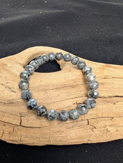 8mm faceted Larvikite beaded stretch bracelet resting on a driftwood display, showing a dark grey matrix and metallic silver flash.