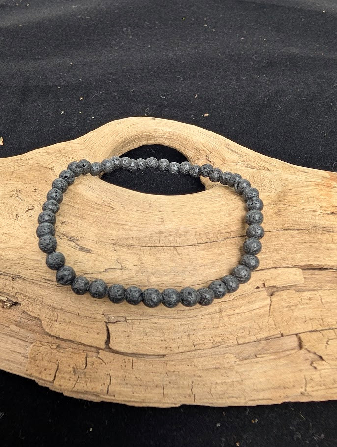 4mm matte black Lava Stone beaded stretch bracelet resting on a driftwood display, showing natural porous texture.