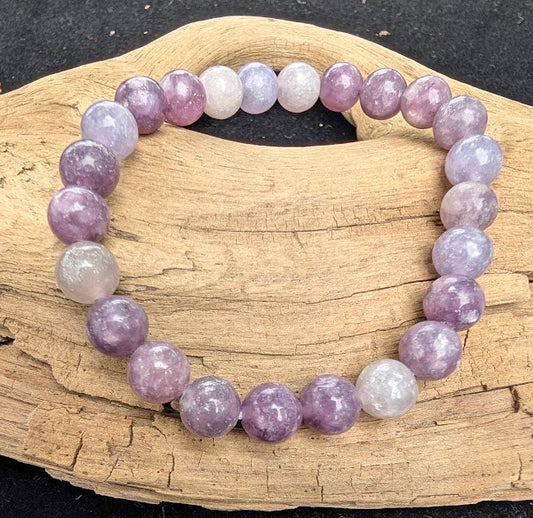 8mm polished Lepidolite beaded stretch bracelet resting on a driftwood display, showing lavender tones and natural silvery mica flash.