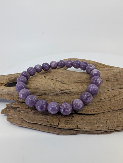 Full 8mm Lepidolite bead bracelet from Brazil displayed on natural driftwood showing rich purple color.