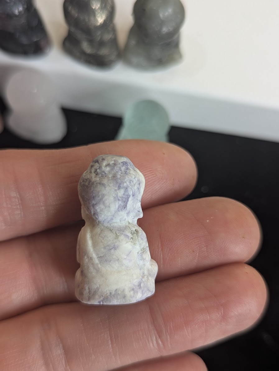 The rear view of a Lepidolite meditating monk totem highlighting the natural purple and white mottled texture of the polished stone.