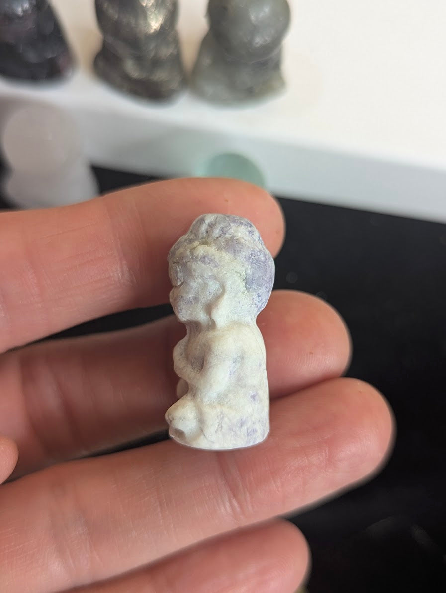 Handheld side profile of a carved Lepidolite meditating monk totem showing the rounded contours of the figure's robes and hands in prayer.