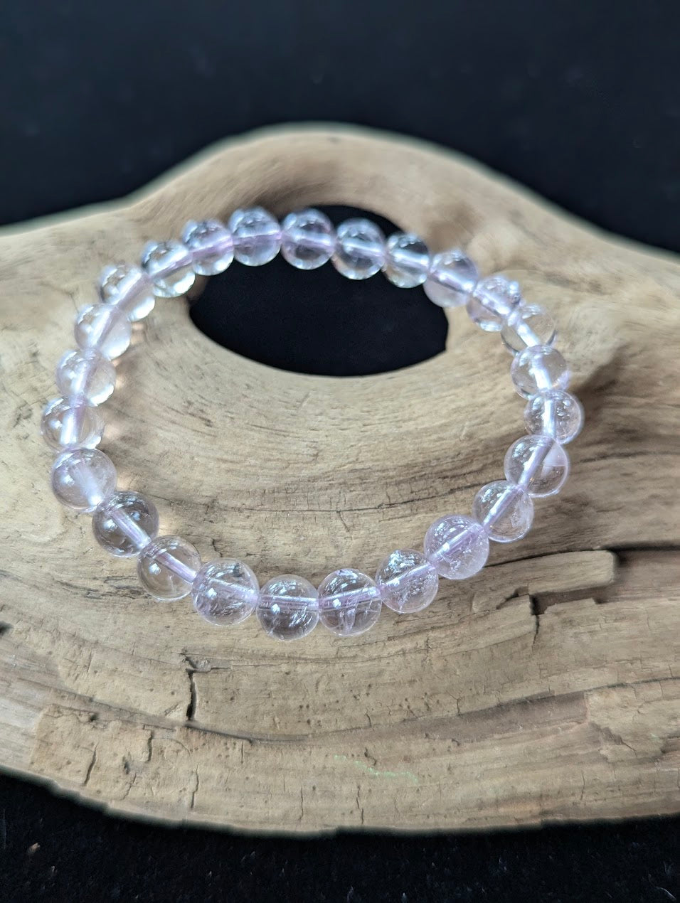 7mm AA Grade Light Amethyst gemstone bracelet from Bolivia resting on natural driftwood, showcasing delicate lavender coloration and high clarity.