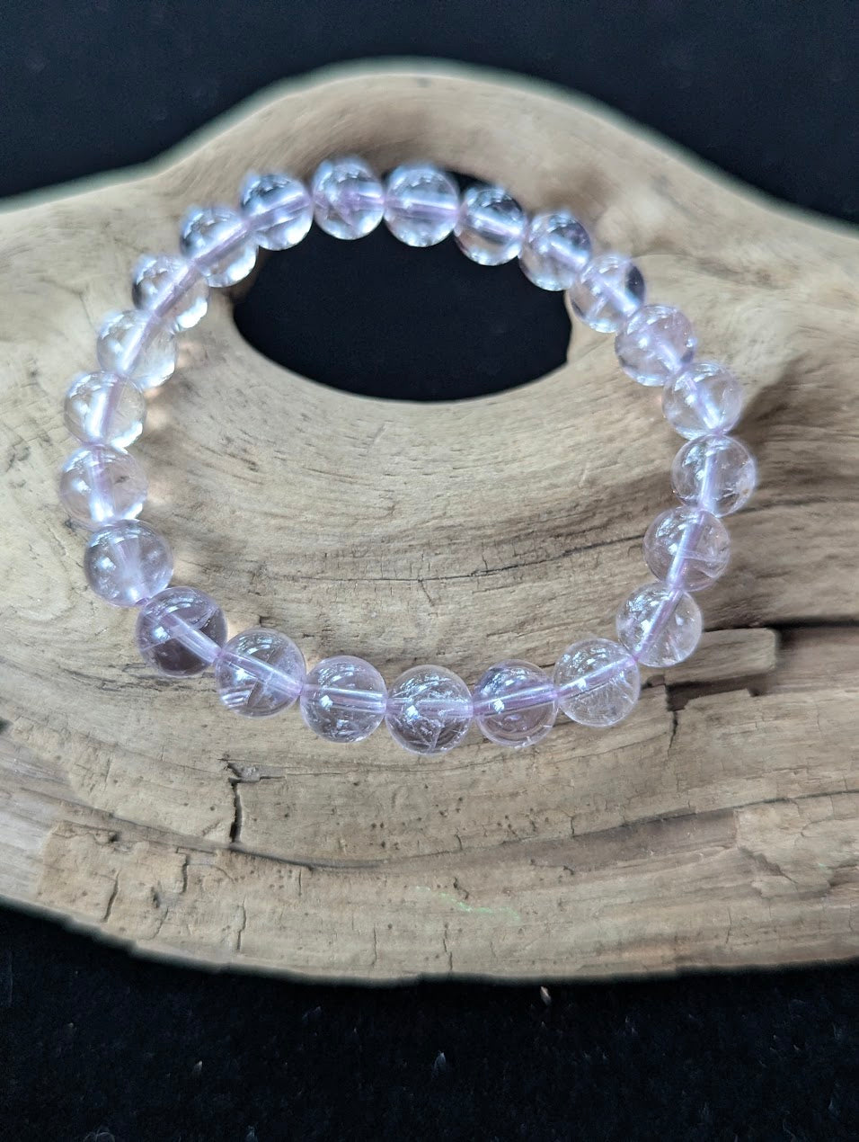 8mm AA Grade Light Amethyst beaded bracelet displayed on textured wood, revealing soft lilac quartz structure.